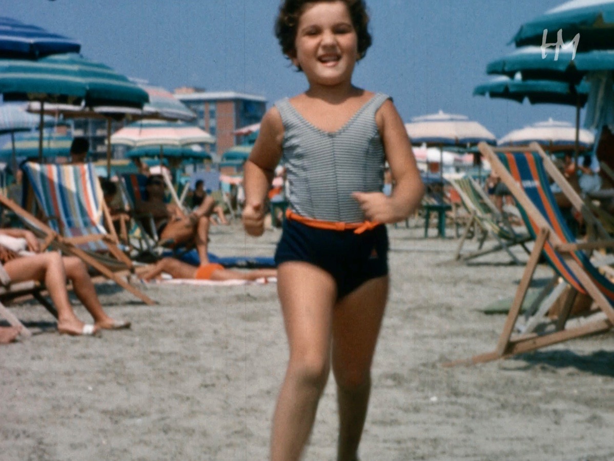 Bambina sulla spiaggia che corre verso l'obiettivo